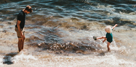 a father and a toddle play at the edge of the surf